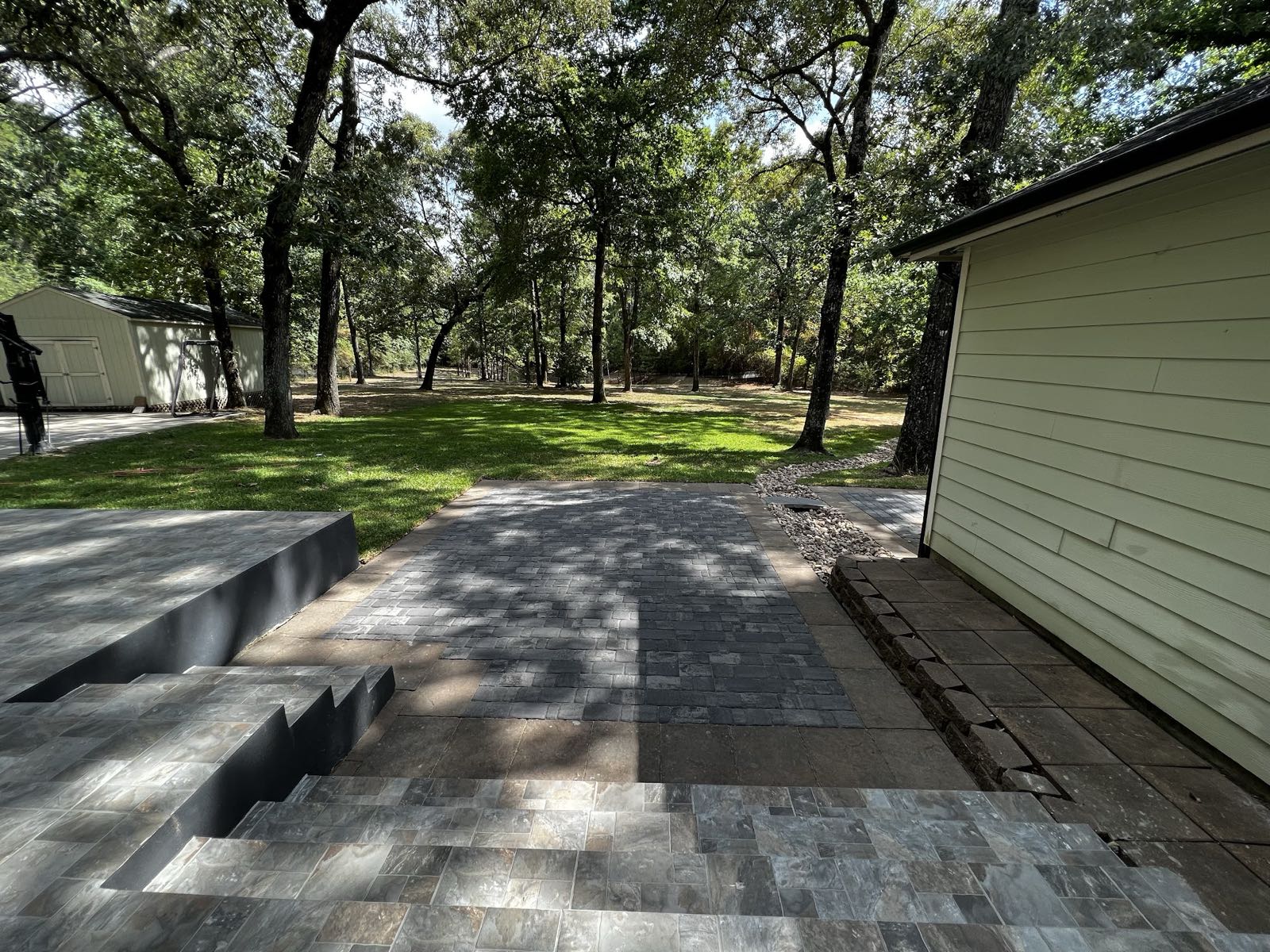 Grey paver patio and steps leading out to a wooded backyard lawn