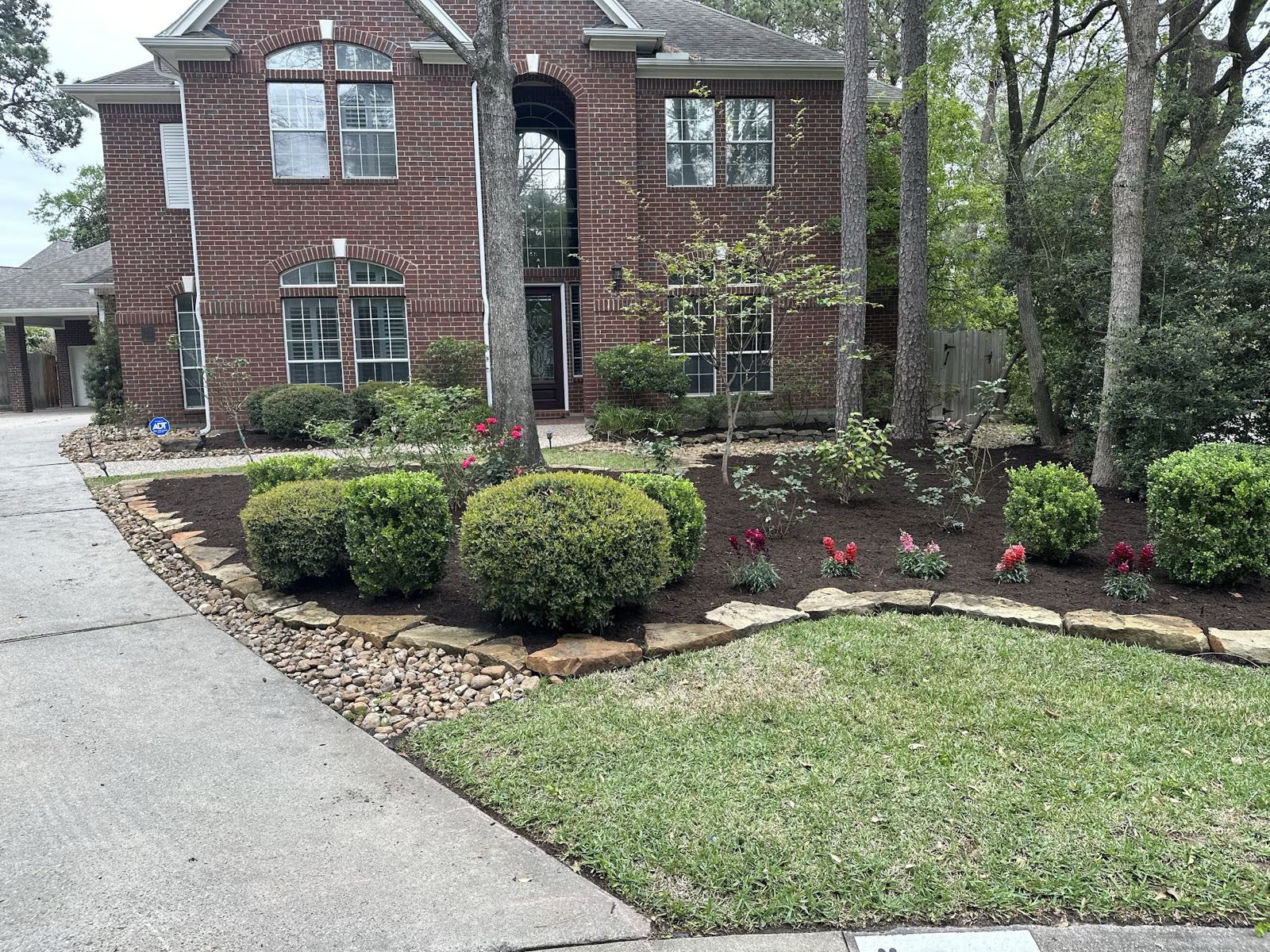 Front bed of rounded shrubs, red flowers and a natural stone border at a brick home