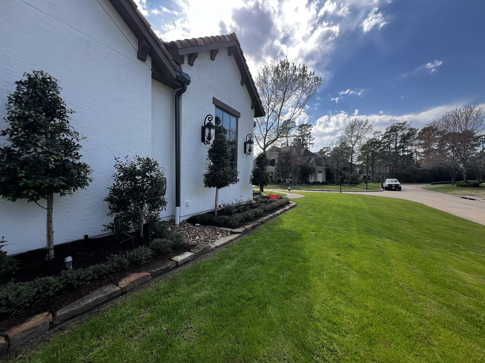 Bright green lawn and shrub bed edged in stone beside a white stucco home
