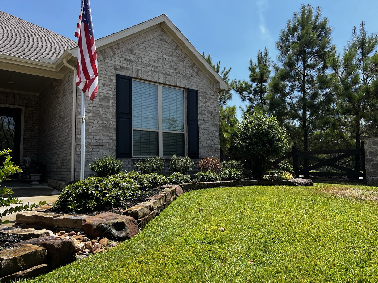 Lush green lawn and natural stone bed border in front of a brick home with a US flag