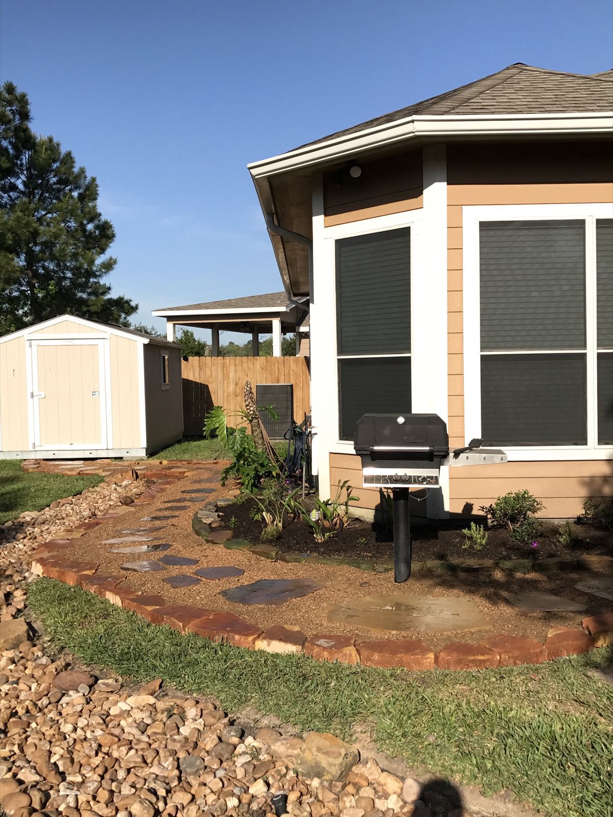 Stepping-stone path through a brick-edged bed with river rock beside a house